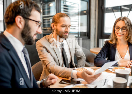 Drei Geschäftsleute arbeiten mit Dokumenten zusammen sitzen während der Kaffeepause in der modernen Cafe innen Stockfoto