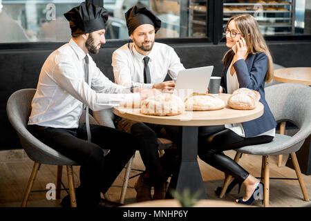 Mit zwei eleganten Bäcker oder Koch Köche arbeiten mit Laptop im Cafe mit Küche auf dem Hintergrund Geschäftsfrau Stockfoto