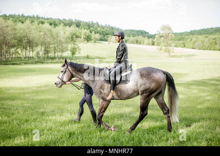 Mann ein Pferd mit Frau Reiter auf dem schönen grünen Wiese während der sonnigen Wetter Stockfoto