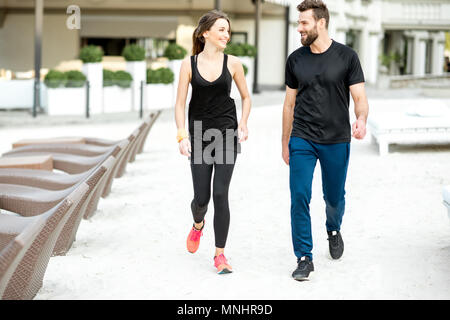 Paar in Schwarz Sportbekleidung Walking am Strand im Resort Stockfoto