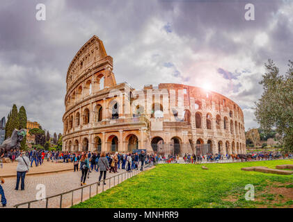 Rom, Italien, 4. März 2017: Touristen gehen unter dem Kolosseum in Rom an einem bewölkten Tag mit der Sonne hinter glänzenden Stockfoto