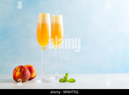 Zwei Gläser Champagner mit einem Cocktail von Bellini und frische Pfirsiche auf einem blauen Hintergrund. Sommer erfrischendes Getränk Stockfoto