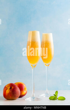 Zwei Gläser Champagner mit einem Cocktail von Bellini und frische Pfirsiche auf einem blauen Hintergrund. Sommer erfrischendes Getränk Stockfoto