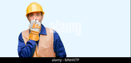 Senior Engineer Mann, Bauarbeiter deckt Mund in Schock, blickt schüchtern, Stille und Fehler Konzepte, erschrocken über Blau isoliert backgrou Stockfoto