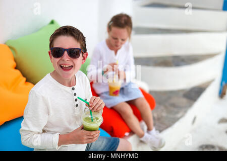 Zwei süße Kinder Bruder und Schwester trinken frische Smoothies auf einer bunten Kissen bei Café im Freien im Sommer Tag Stockfoto