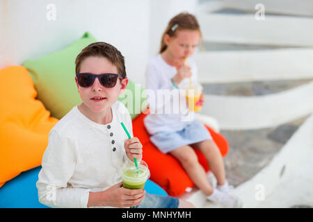 Zwei süße Kinder Bruder und Schwester trinken frische Smoothies auf einer bunten Kissen bei Café im Freien im Sommer Tag Stockfoto