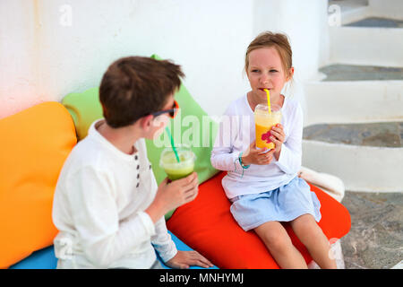 Zwei süße Kinder Bruder und Schwester trinken frische Smoothies auf einer bunten Kissen bei Café im Freien im Sommer Tag Stockfoto