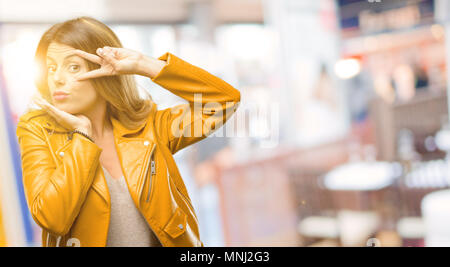 Schöne junge Frau an der Kamera durch ihre Finger im Sieg Geste zwinkerndes Auge und bläst einen Kuss im Restaurant suchen Stockfoto