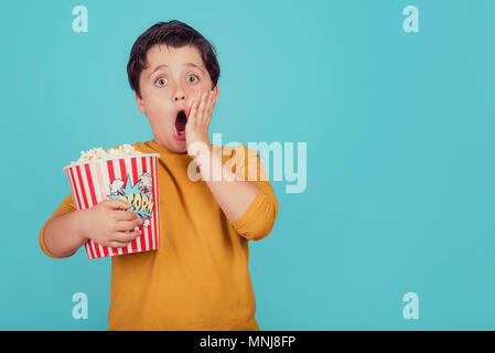 Überrascht Junge mit Popcorn auf blauem Hintergrund Stockfoto