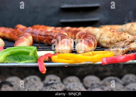 Leckeres Essen, Ernährung, kulinarischen und Grill Konzept: gegrillte Würstchen, Hähnchen Schenkel und Gemüse auf einem Grill. Stockfoto