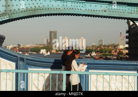 Zwei junge Frauen überschreiten die Tower Bridge, London zu Fuß mit einem Blick in Richtung Osten Londons an einem sonnigen Abend mit Teile aus Metall ist die Bridge unterstützt Stockfoto