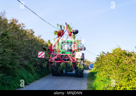 Traktor mit einer Reihe von Spinnern auf der Rückseite auf einem Feldweg in Irland nach dem Einschalten über Gras für Silage. Stockfoto