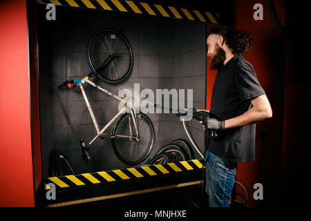 Services Professional Waschen ein Fahrrad in der Werkstatt. Nahaufnahme der Hand jungen kaukasischen stilvollen Mann tun, Fahrradverleih, Reinigung mit Automatische elektrische Wasserpumpe. Sprays streuen den Druck Stockfoto