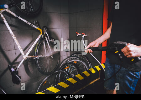 Services Professional Waschen von Fahrrad in die Werkstatt. Nahaufnahme der Hand jungen kaukasischen stilvollen Mann tun, Fahrradverleih, Reinigung mit Hilfe eines automatischen elektrischen Wasserpumpe. Sprays streuen den Druck Stockfoto