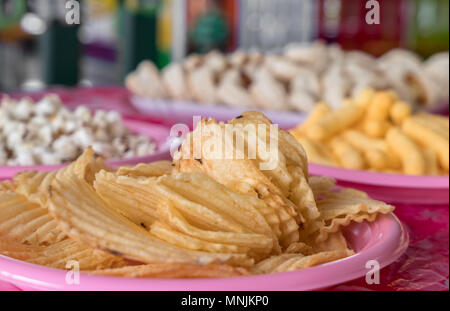 Junk Food für Party, Geburtstag, jedes Event. Im Vordergrund wellig Kartoffelchips. Im defokussierten Hintergrund, Popcorn und mini Pizzen. Stockfoto