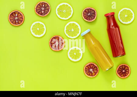 Schönes essen Kunst Hintergrund. Gelbe und rote Saft in Glasflaschen in Scheiben geschnittenen Zitrone und orange Frucht auf helle grüne Fläche. Stockfoto