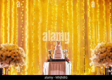 Schöne vier Schichten Hochzeit auf dem Tisch auf der Bühne Dekoration mit LED-Leuchte in Gelb golden Thema mit Teil der biuquet Blume verschwommen im Vordergrund Stockfoto