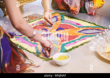 Frauen hilft Färbung Tradition bunte Reis Kunst oder sand Kunst (RANGOLI) auf dem Boden mit Papier Muster mit trockenem Reis und Mehl mit farbigen aus Stockfoto