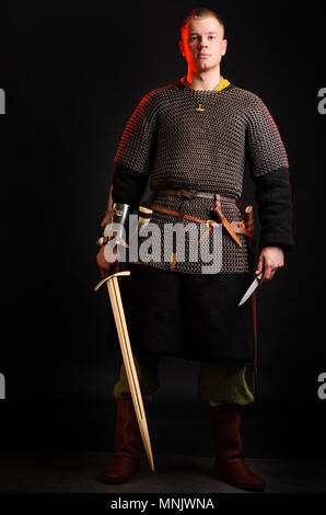 Ein Soldat in einer Kette von Buchstaben steht mit einem Schwert in der Hand auf einem schwarzen Hintergrund. Stockfoto
