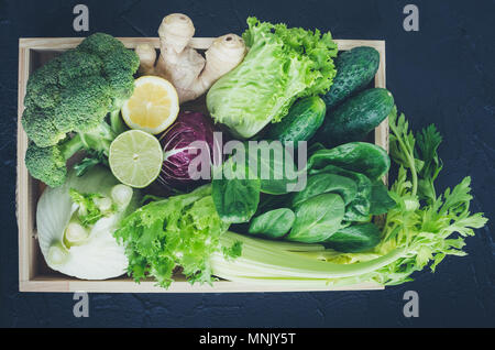 Sortiert grün und lila frisches Gemüse, grünen und Frucht in Holz- Fach auf schwarzem Hintergrund. Detox Diäten, sauber essen, vegetarisch, vegan, Fitne Stockfoto