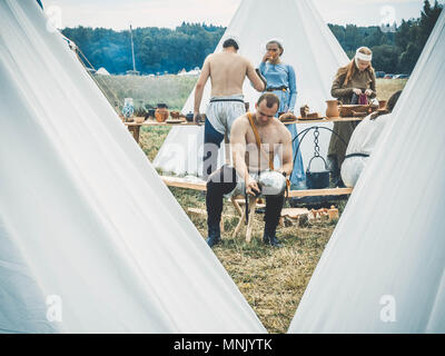 RITTER WEG, MOROZOVO, APRIL 2017: Outdoor Szene des mittelalterlichen Lebens. Der Kerl reinigt den Helm nach einem Kampf der Ritter improvisiert. Im Hintergrund, ein Feld, eine Küche und ein mittelalterliches Lager. Stockfoto