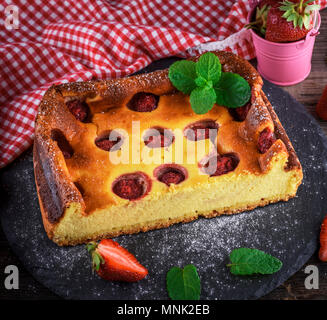 Die Hälfte einen Käsekuchen mit Erdbeeren auf schwarzem Graphit Platte mit einem grünen Zweig Minze, Nahaufnahme Stockfoto