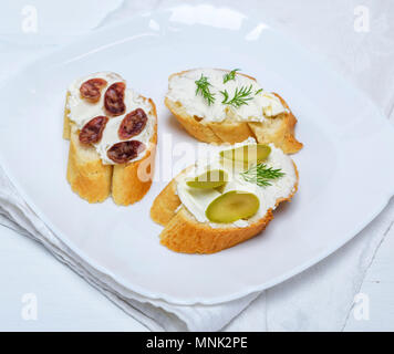 Sandwiches mit cremiger Käse, Wurst, Oliven und Dill auf einem weissen Teller, Holz- weißer Tisch Stockfoto