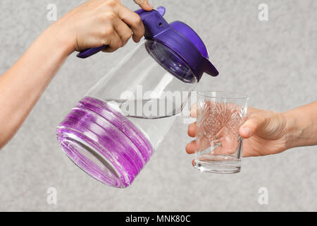 Hände goß Wasser aus einem Krug in ein Glas von einer anderen Person Stockfoto