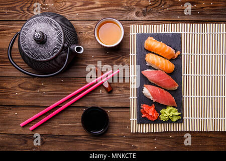 Sushi Set serviert auf grauem Stein Schiefer mit Sojasoße, grau Teekanne und Tasse Tee Stockfoto