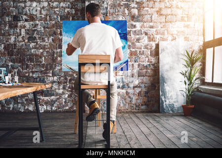 Männliche Maler sitzt auf Stuhl vor die Leinwand und Zeichnung Bild im Studio. Kunst klasse und Werkstatt. Künstler malen. Hobby Stockfoto