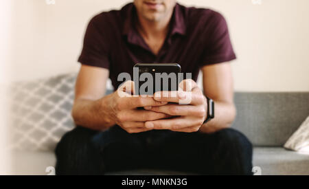 Der Mann bei der Arbeit am Handy sitzt auf einem Sofa. Mann das Handy mit zwei Händen. Stockfoto