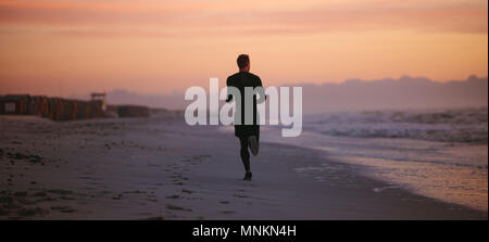 Ansicht von hinten erschossen von fit Mann laufen am Ufer des Meeres am Morgen. Gesunde männliche Athleten am Strand entlang läuft. Stockfoto