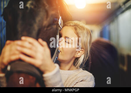 Lächelnde junge Frau, die in einem stabilen liebevoll ihr Kastanie Pferd umarmte, bevor Sie für eine Fahrt Stockfoto