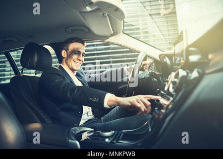 Lächelnde junge Unternehmer trägt einen Blazer ändern Radiosender, während sein Auto durch die Stadt fahren während seiner Morgen pendeln zur Arbeit Stockfoto