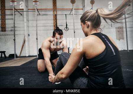 Passen junge Mann seine Übung Partner helfen die USV auf dem Boden einer Turnhalle während eines Training Session zusammen sitzen Stockfoto