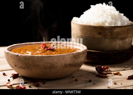 Nahaufnahme einer Schüssel mit einem Chicken Korma Curry und eine Schüssel mit gekochten Reis auf einem Off-white Holztisch Stockfoto