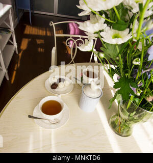 Sonniges Wohnzimmer mit einem großen Blumenstrauß auf dem runden Tisch, Interieur im Stil der Provence Stockfoto