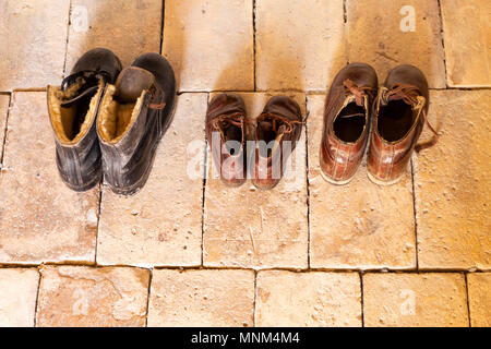 Blick von oben auf die drei Paar alte, abgetragene Schuhe aus Leder in einer Linie auf beige Stein. Stockfoto