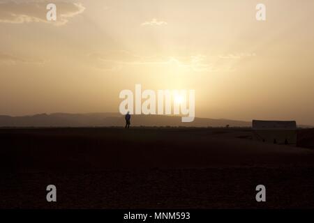 Einer Person, die auf einer Sanddüne beobachten Sie den Sonnenuntergang über der Wüste Zagora, Marokko Stockfoto