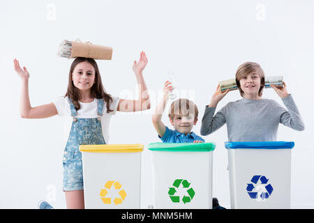 Glückliche Kinder Spaß haben, während die Trennung von Hausmüll in Behälter mit Recycling Symbol auf weißem Hintergrund Stockfoto