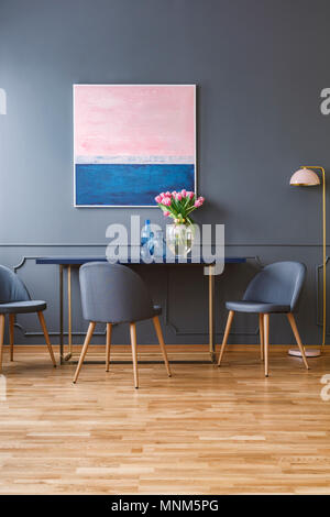 Hölzerne Stühle am Tisch mit rosa Blüten im eleganten Speisesaal Interieur mit Malerei und Lampe Stockfoto