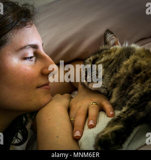 Eine Nahaufnahme eines intimen Blick zwischen wunderschönen Persischen tricolor Katze, mit erstaunlichen Fell und eine Frau, zwei Ringe, mit einem natürlichen Licht, auf einem Bett. Stockfoto