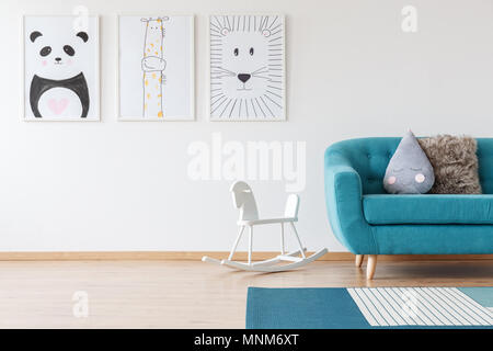 Kid's Zeichnungen an der Wand und weiß Schaukelpferd in Blau Wohnzimmer mit Kissen auf der Couch und Teppich Stockfoto