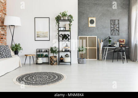 Runde gemusterten Teppich im geräumigen Wohnzimmer mit Pflanzen, Poster und Arbeitsbereich gegen graue Wand Stockfoto