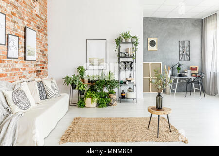 Hocker mit Vase auf braunen Teppich im hellen Wohnzimmer mit weißen Sofa und Pflanzen Stockfoto