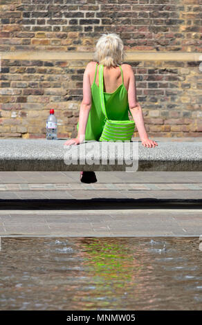 Junge Frau in einem grünen Kleid entspannende durch Wasser im Getreidespeicher Square, Parkside, King's Cross, London, England, UK. Stockfoto