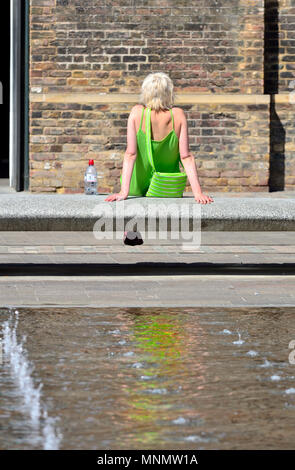 Junge Frau in einem grünen Kleid entspannende durch Wasser im Getreidespeicher Square, Parkside, King's Cross, London, England, UK. Stockfoto