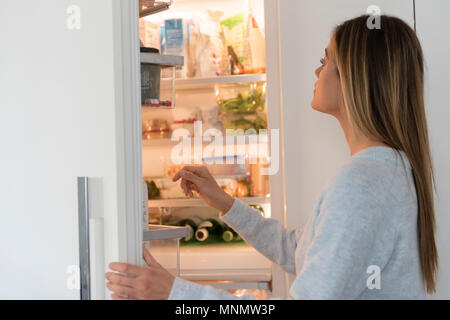 Junge Frau sucht in Kühlschrank Stockfoto