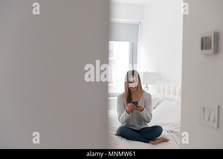 Junge Frau im Bett sitzen und mit smart phone Stockfoto