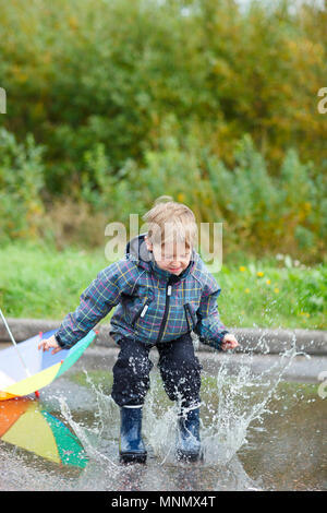 Verspielte Junge in der Pfütze springen an regnerischen Herbsttag Stockfoto